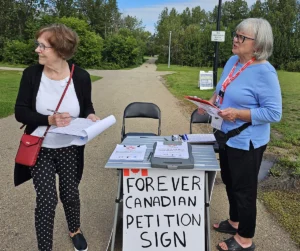 Volunteers collecting signatures at a Forever Canadian petition table in a park setting.