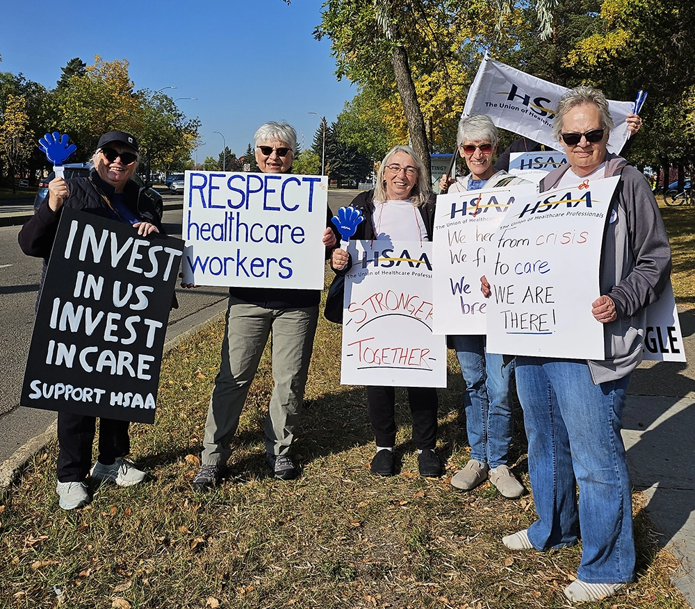 Healthcare workers holding signs including “Respect healthcare workers” and “Invest in care” at roadside rally