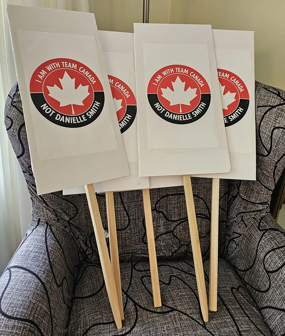 Protest signs reading “I Am With Team Canada Not Danielle Smith” prepared in advance of a roadside rally.