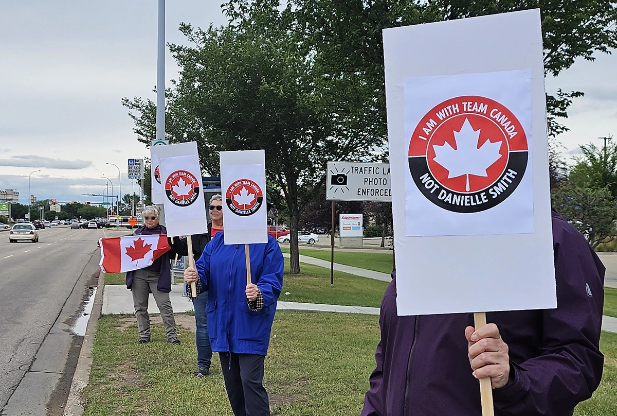 Members of our group stand along a roadside in St. Albert holding signs reading “I Am with Team Canada Not Danielle Smith.”