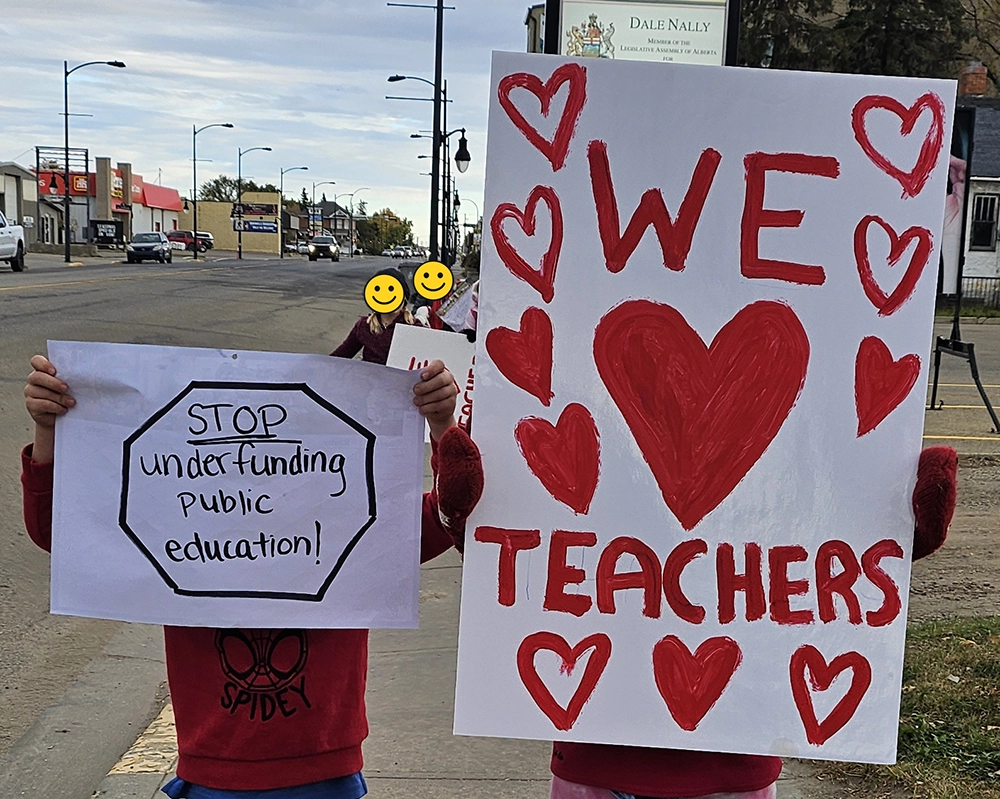 Children holding signs reading “We love teachers” and “Stop under-funding public education”